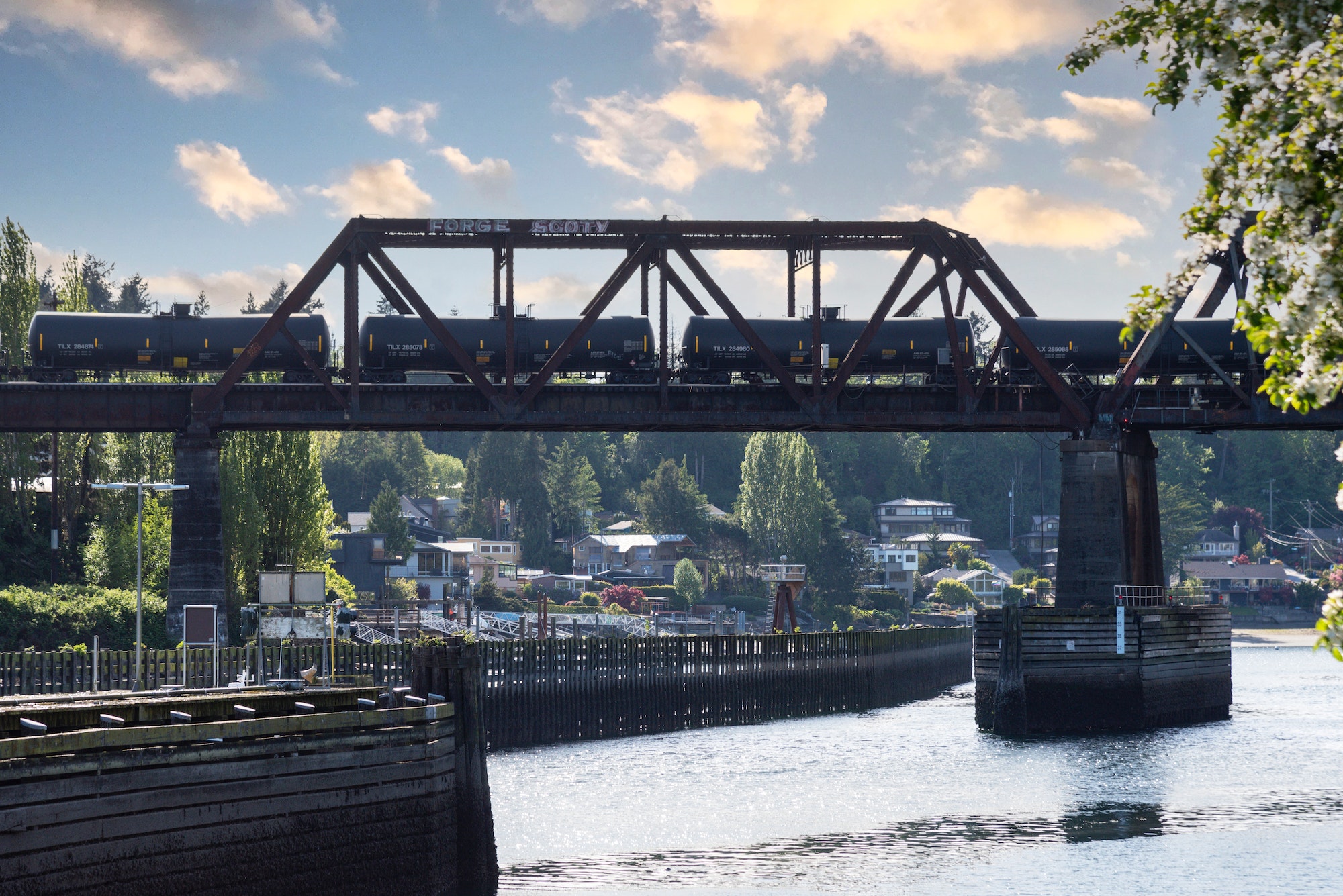 Oil liquid container train cars passing over a waterway on a bridge.